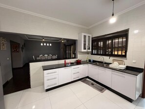 A modern kitchen with white cabinets, a black countertop, and a window with blinds. - Luxury Executive Residence (Maputo)