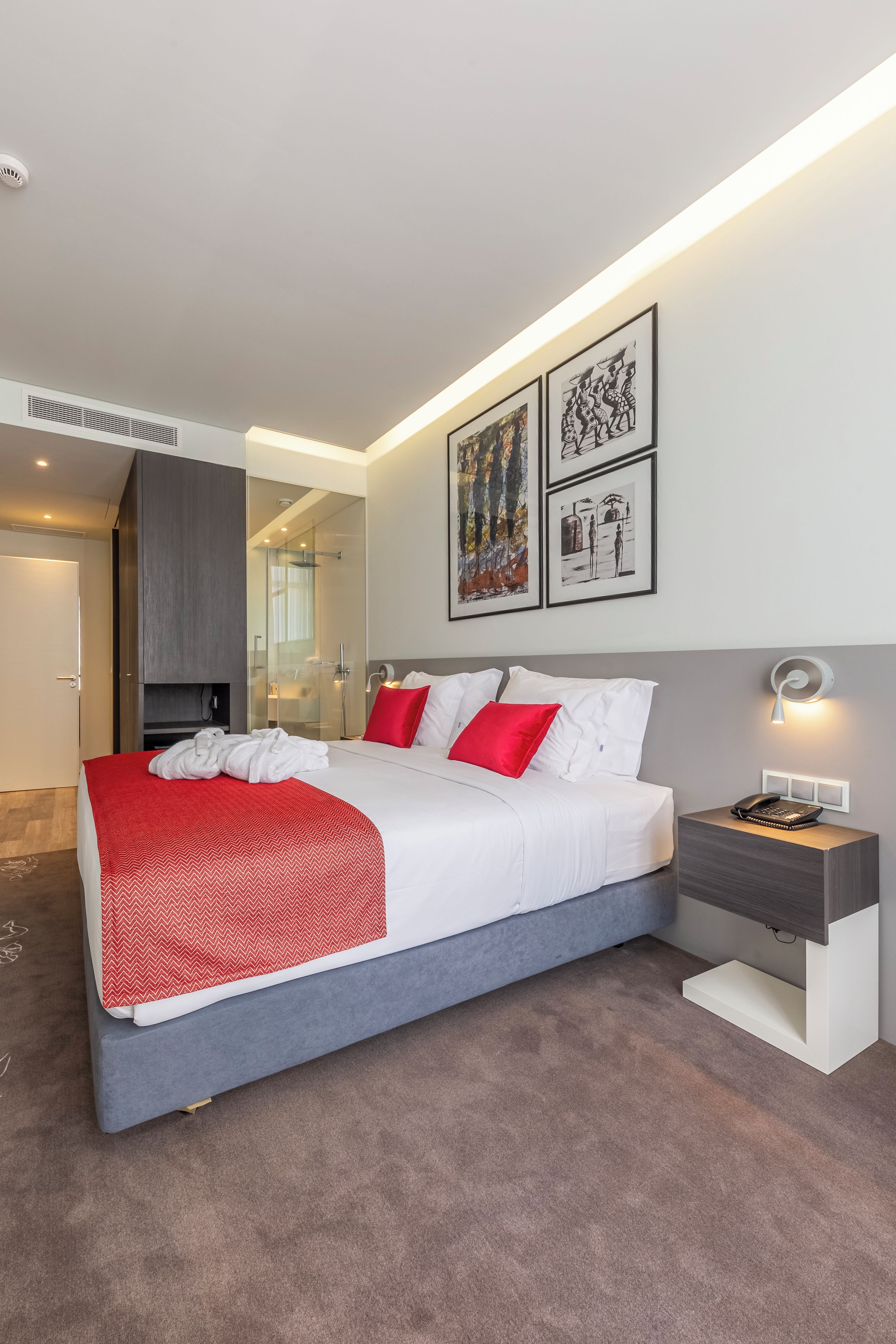 A modern hotel room with a large bed, a bedside table with a lamp, and artwork on the wall.