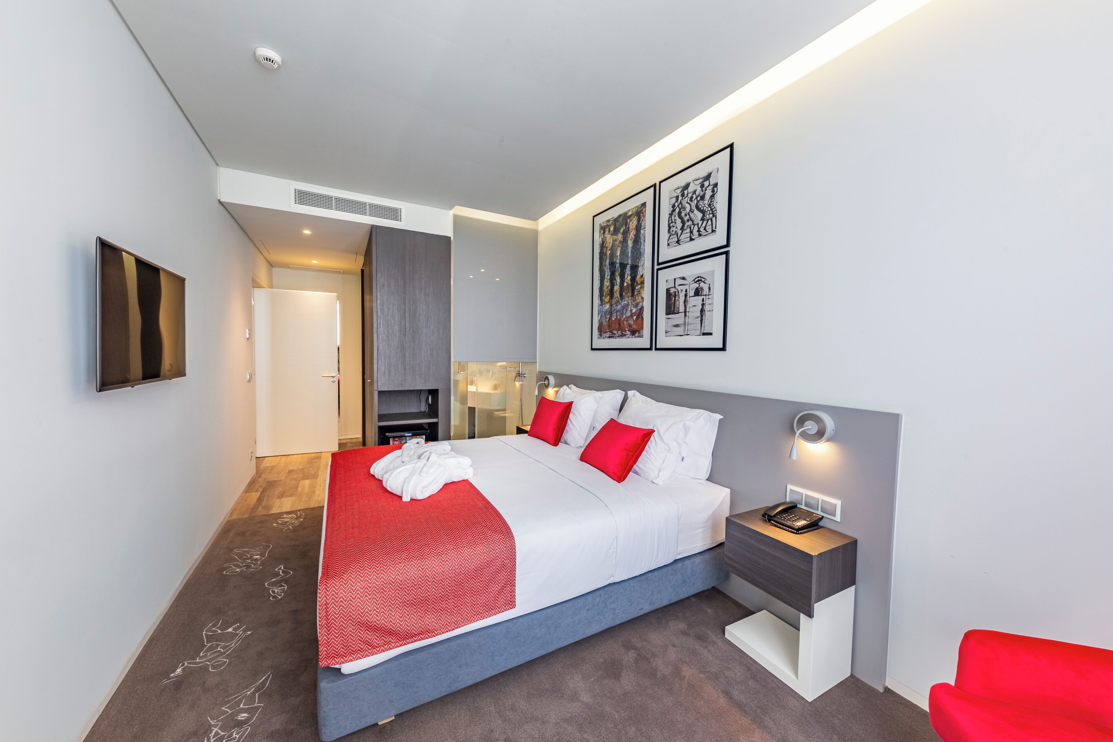 Quarto de hotel moderno com uma cama grande, mesa de cabeceira com abajur e obra de arte na parede.