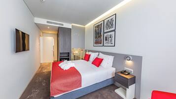 Quarto de hotel moderno com uma cama grande, mesa de cabeceira com abajur e obra de arte na parede.