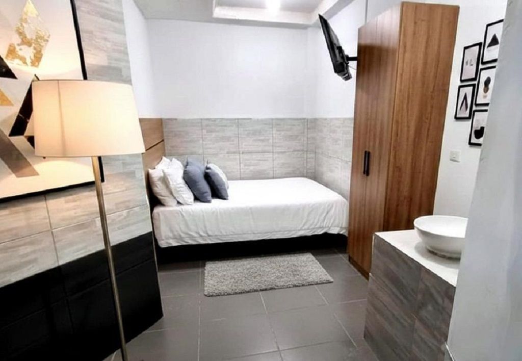 Ein Schlafzimmer mit Bett, Nachttischlampe, einem Holzschrank und einem Badezimmer inklusive Waschbecken.