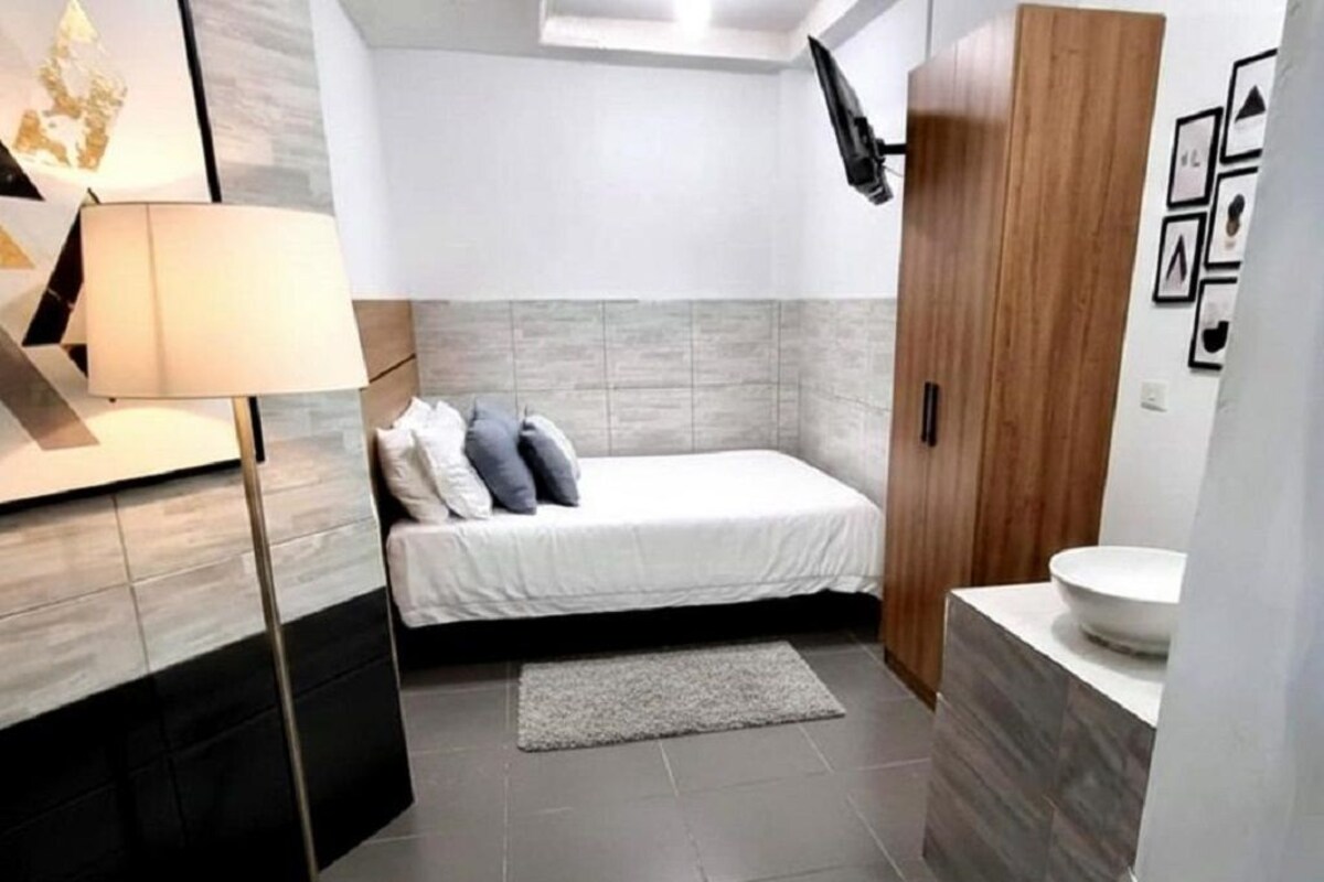A bedroom with a bed, a bedside lamp, a wooden wardrobe, and a bathroom with a sink.