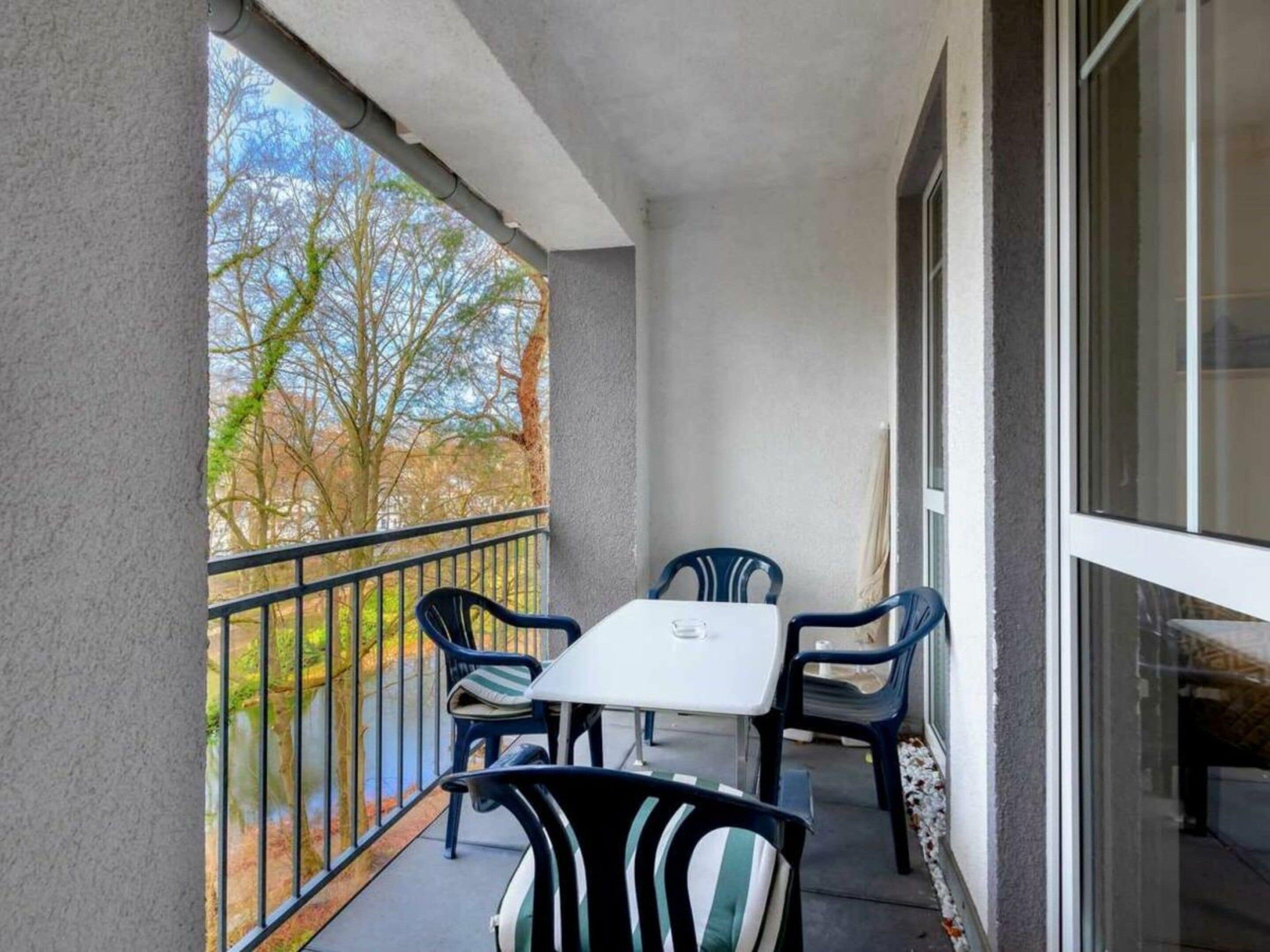 Un balcon avec une table et des chaises, une vue sur les arbres et un bâtiment en arrière-plan.