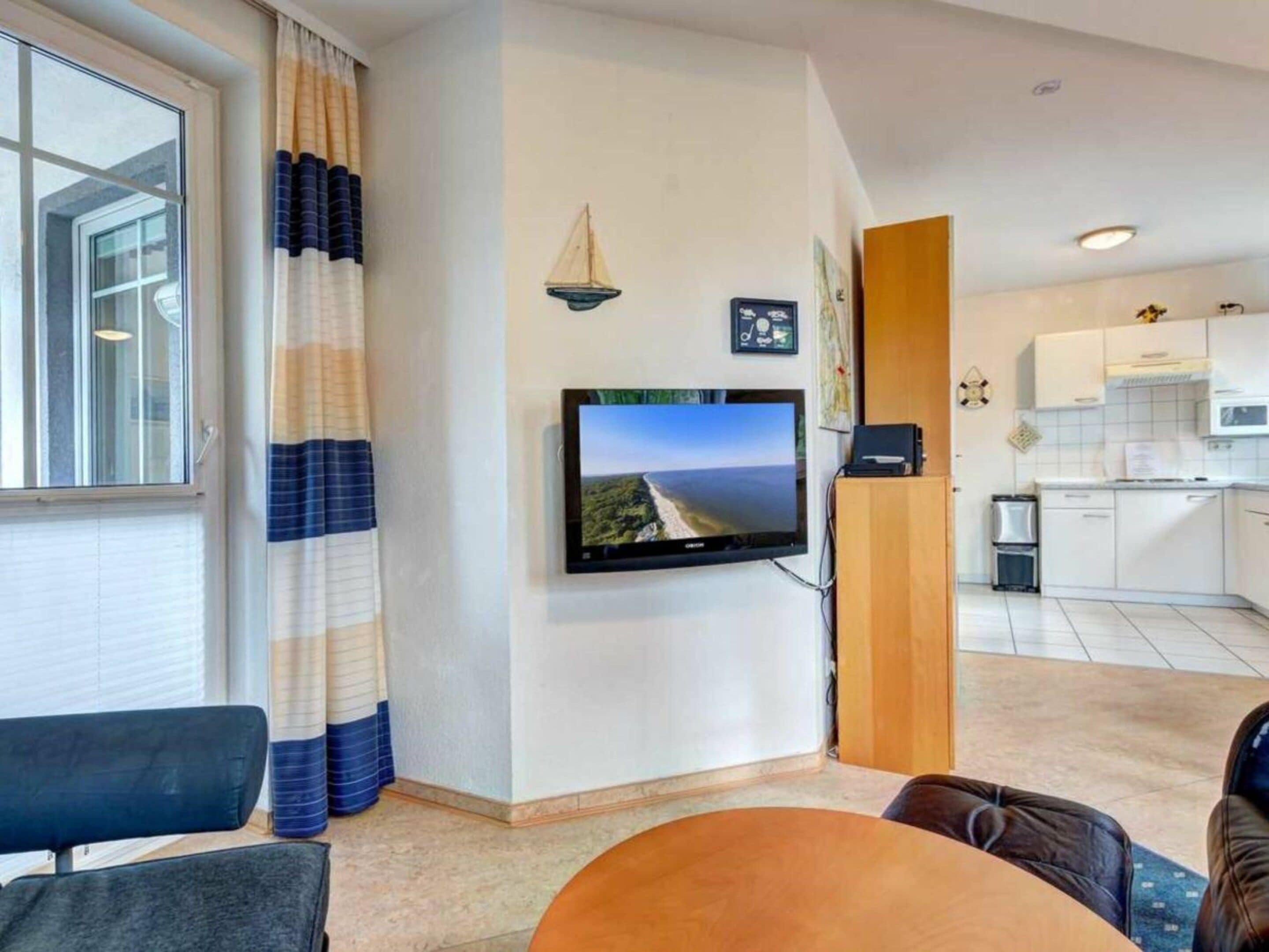 A living room with a television, a dining table, and a kitchen in the background.