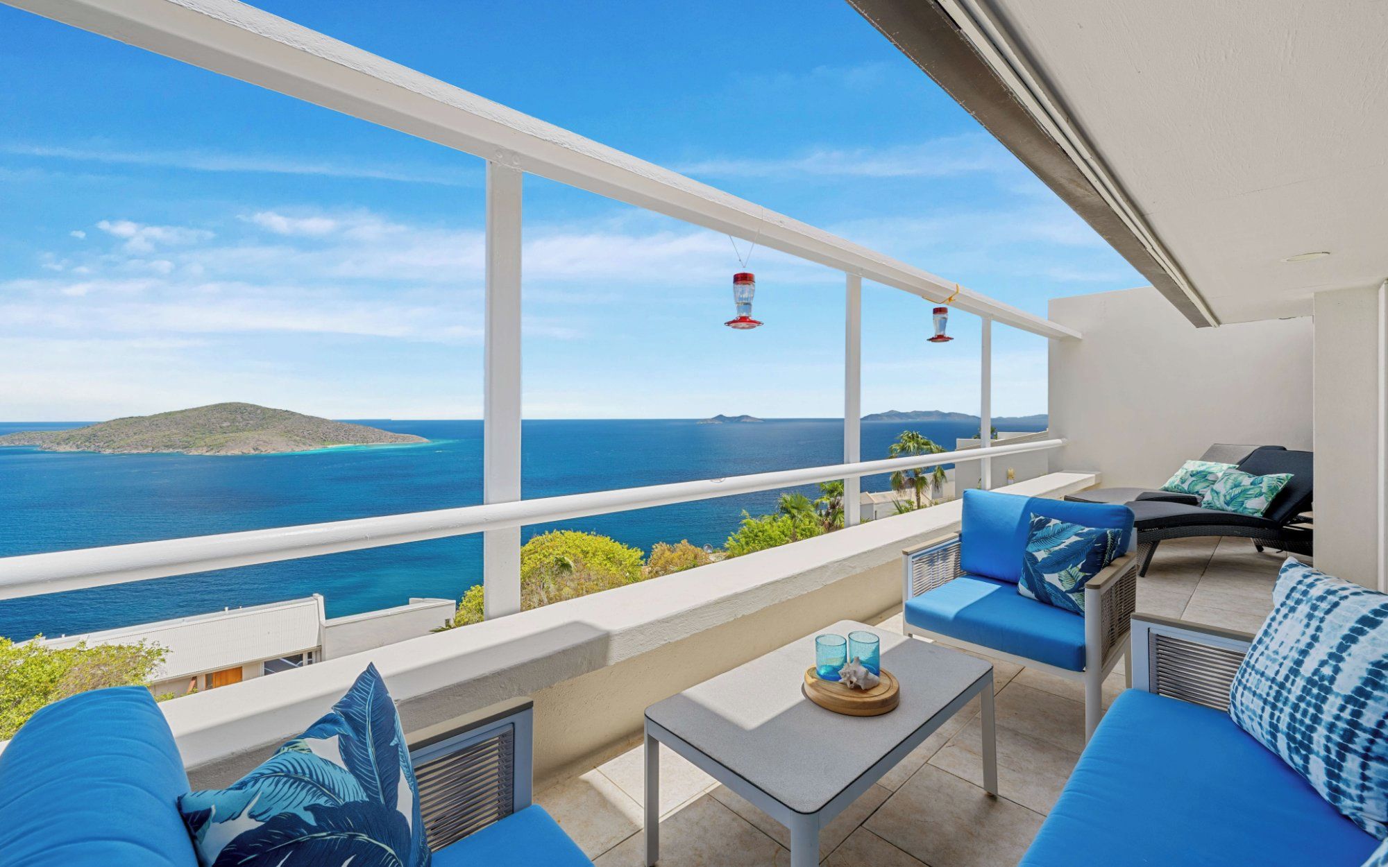 A balcony with a view of the sea, blue cushions, a small table, and a chair.