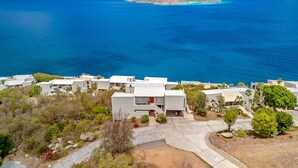 Una zona residenziale sulla costa con edifici bianchi moderni, un mare cristallino e una piccola isola all'orizzonte.