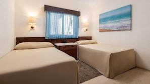 Habitación de hotel con dos camas, una mesita de noche, ventana con cortinas, lámparas fijadas a la pared y una pintura de playa.