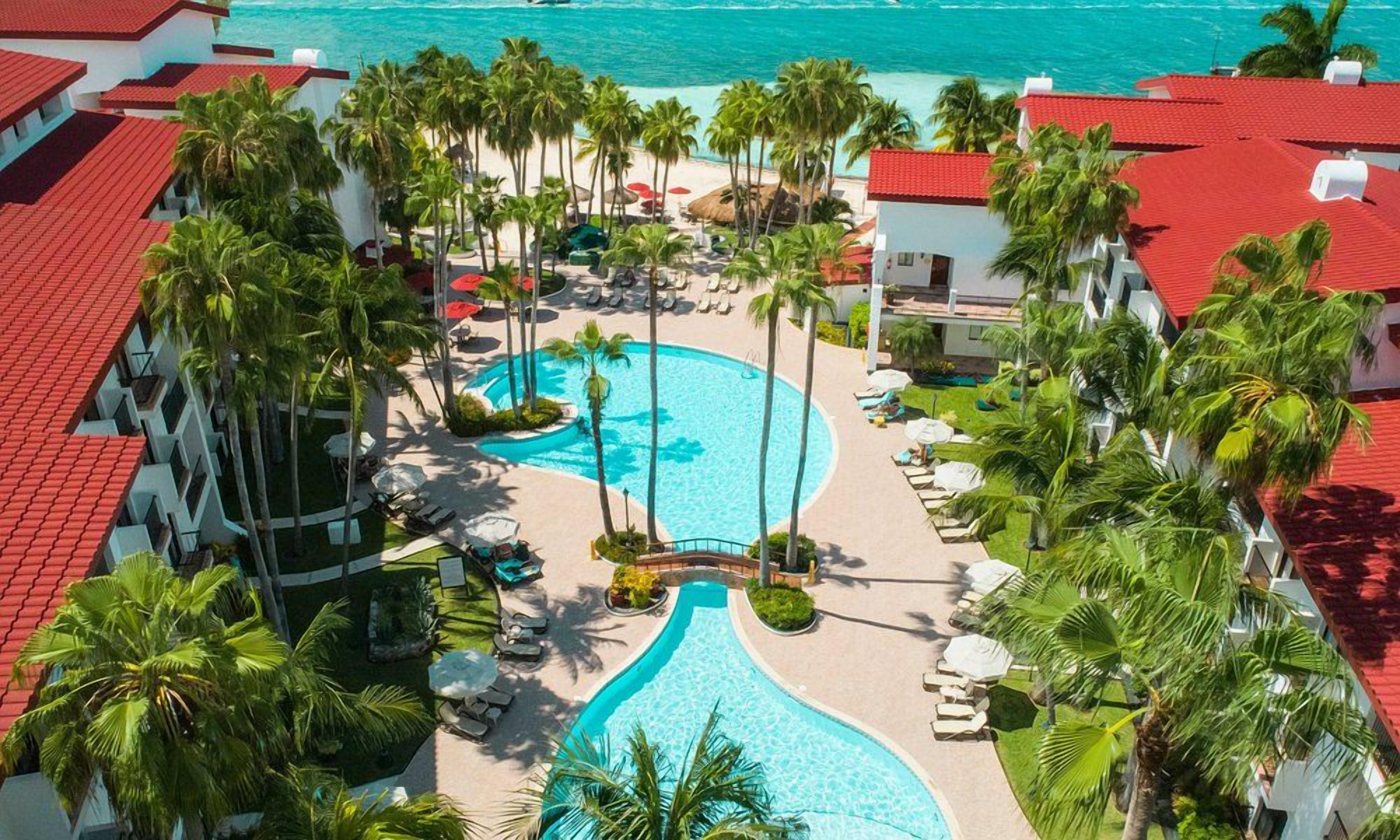 Een resort met een zwembad, palmbomen en uitzicht op de oceaan.