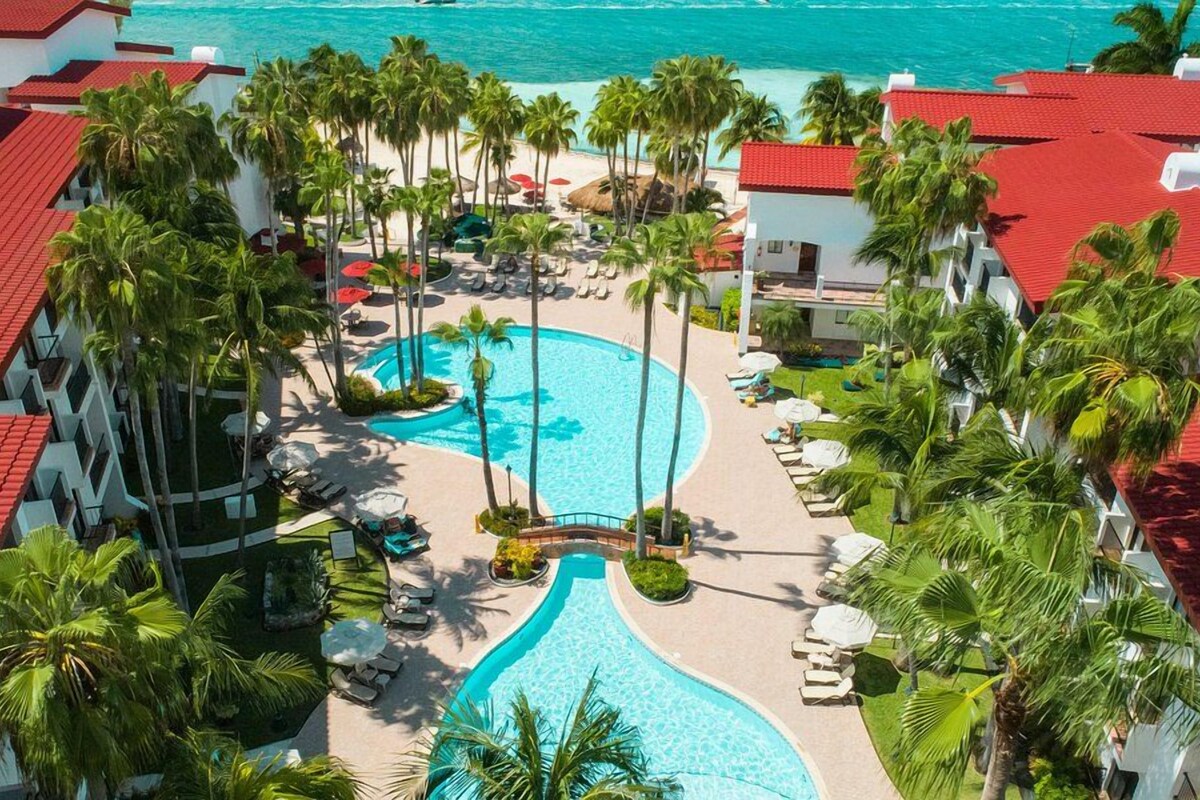 Um resort com piscina central, palmeiras e vista para o oceano.