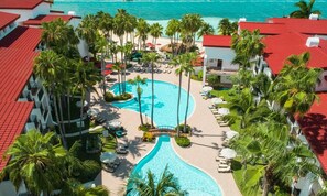 Um resort com piscina central, palmeiras e vista para o oceano.