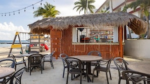 Un bar frente al mar con techo de paja, mesas al aire libre y vista al océano.