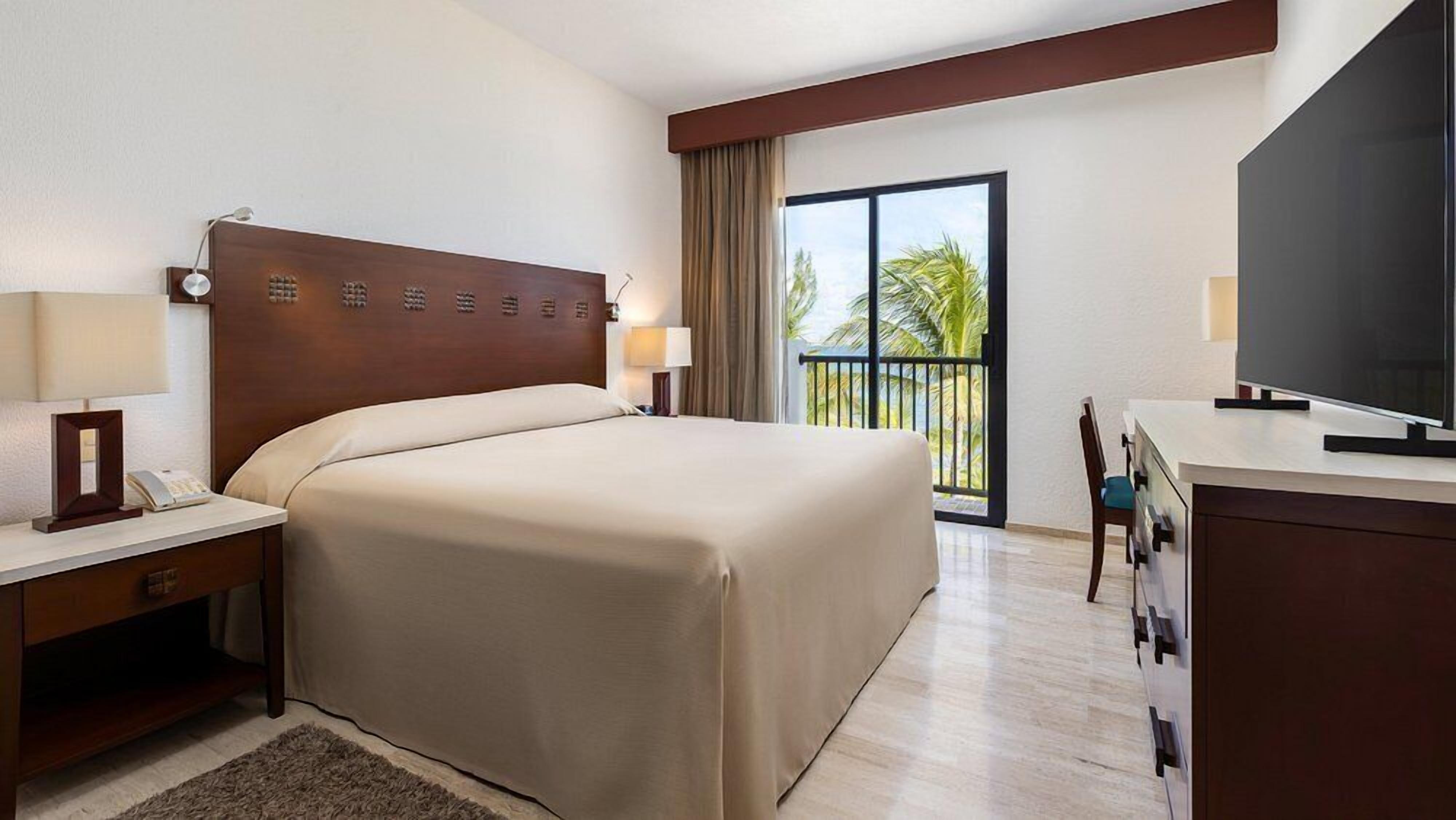Une chambre d’hôtel avec un grand lit, un bureau doté d’une télévision à écran plat, une chaise et un balcon avec vue.
