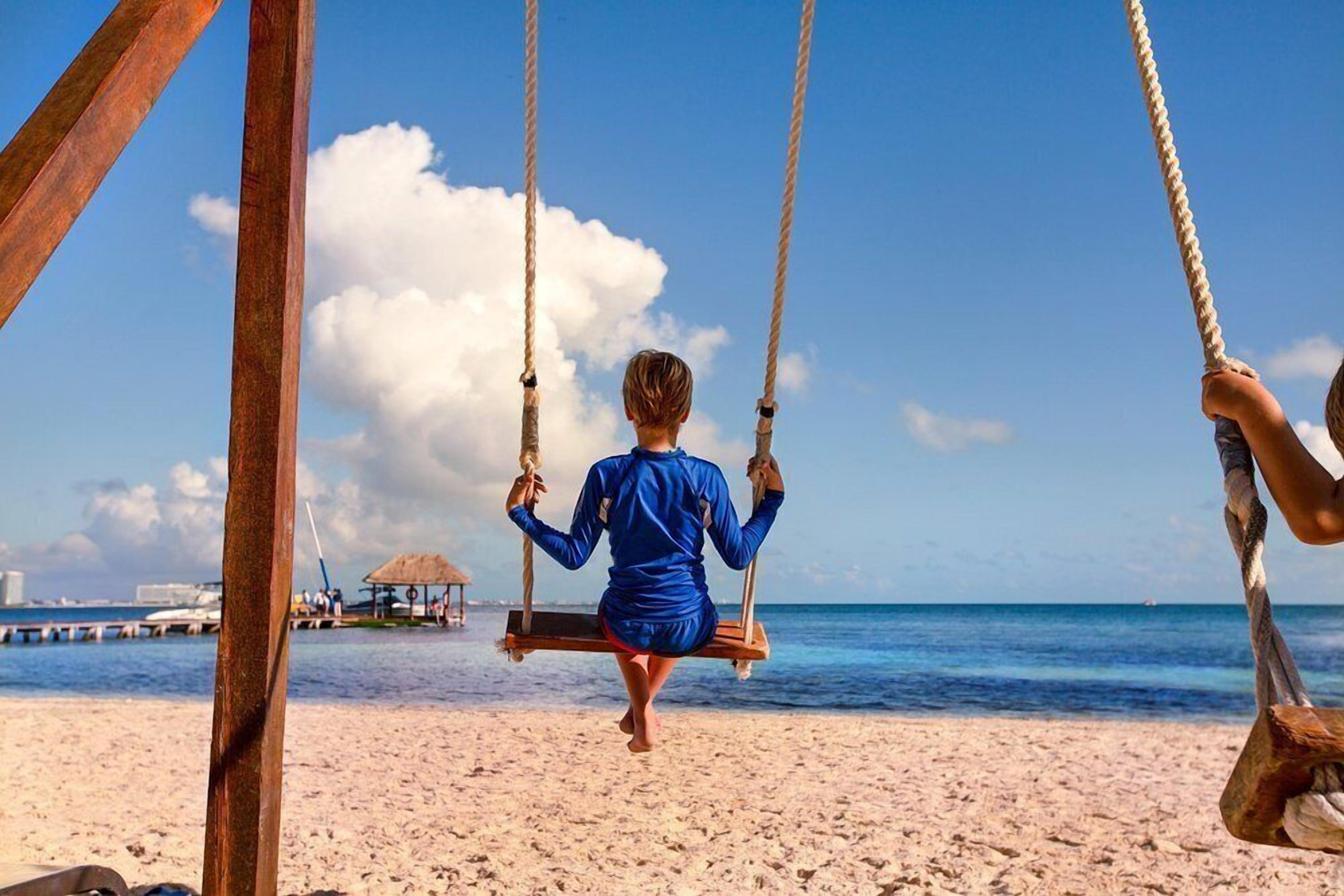 Eine Strandansicht mit einer Schaukel, einer Person, die darauf sitzt, und blauem Himmel.