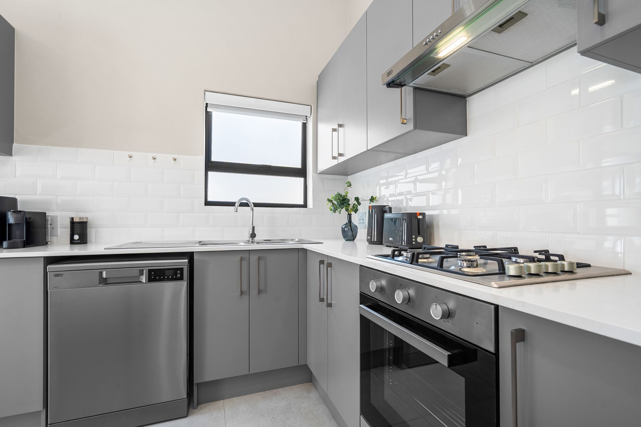 A modern kitchen with stainless steel appliances, a window, and white tiled walls.