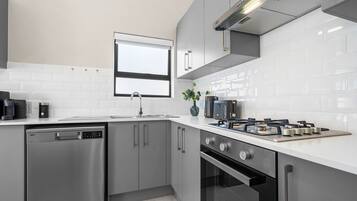 A modern kitchen with stainless steel appliances, a window, and white tiled walls.