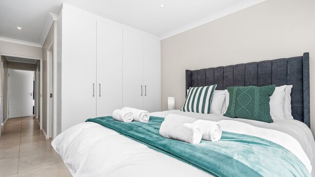 Ein Hotelzimmer mit einem großen Bett, weißen Vorhängen, einem grauen Kopfteil und einer türkisfarbenen Decke.