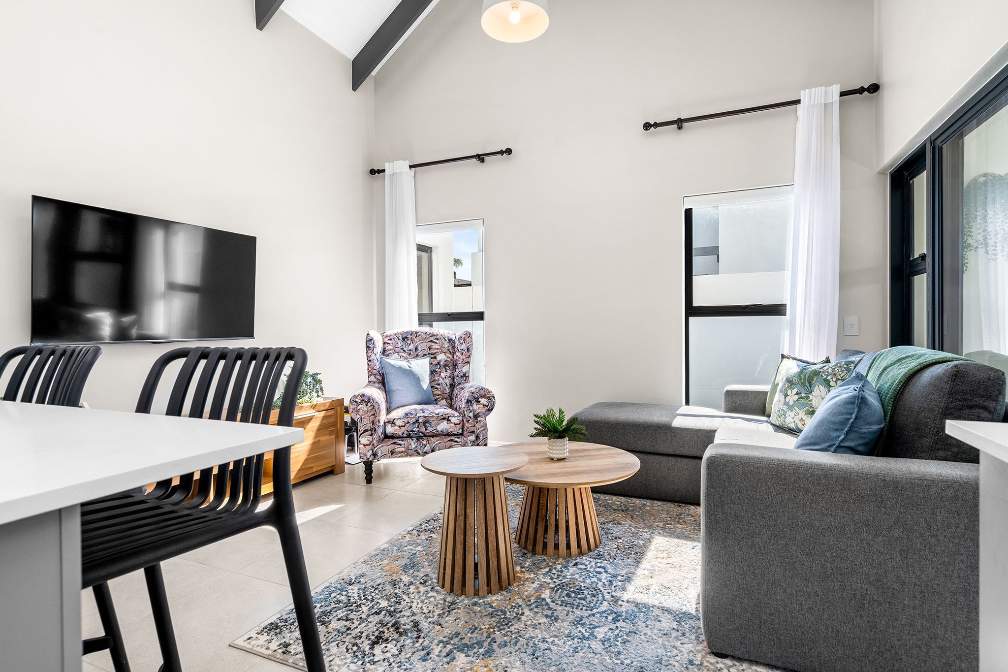 A modern living room with a flat-screen TV, a dining table with chairs, a sofa, a patterned armchair, and a coffee table.