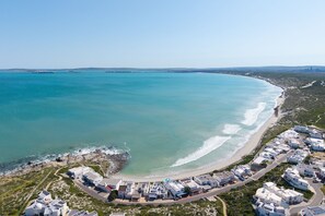 An aerial view of a coastal area with a beach, a rocky shoreline, and a cluster of white buildings with flat roofs. - Langebaan Wildflower (Langebaan)