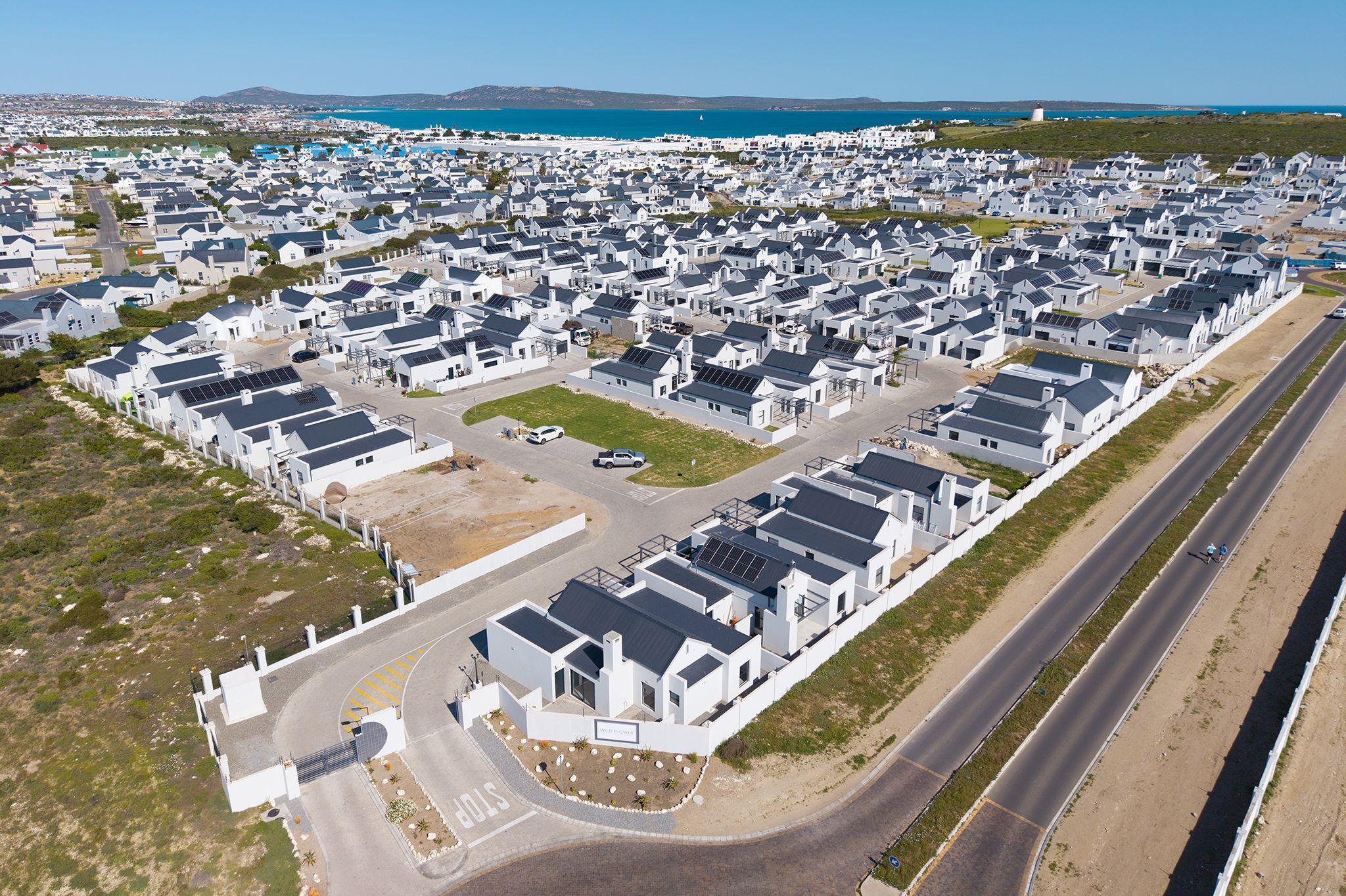 A residential area with modern houses, a road, and a body of water in the background.