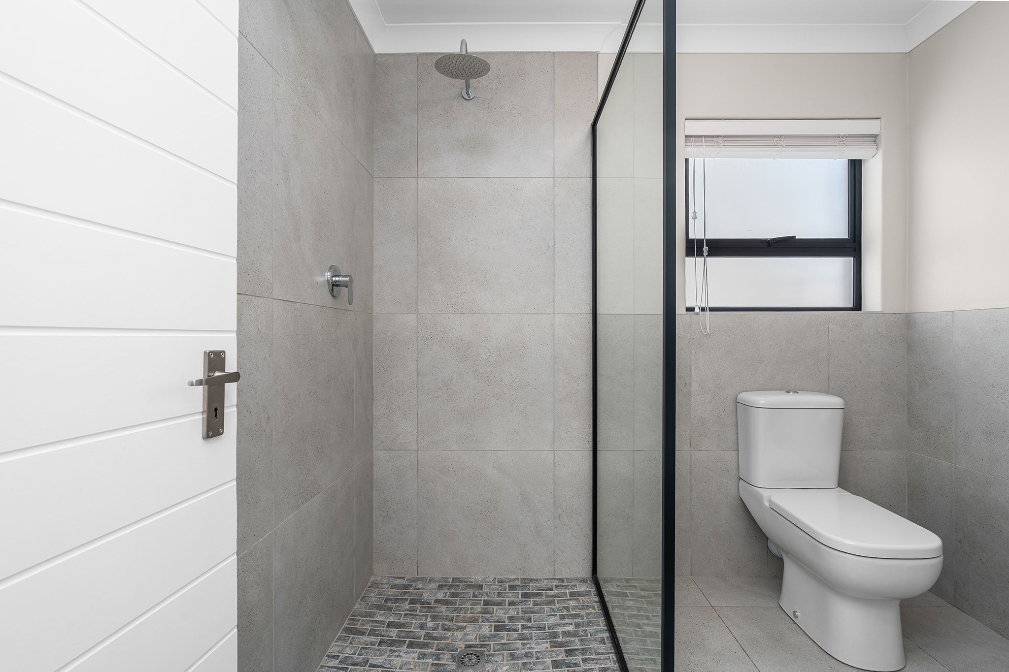 A modern bathroom with a shower, toilet, and a window.