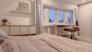 A bedroom with a bed, a desk, a chair, a radiator, and a window with curtains. - Stayplace No. 3: Spacious Hygge Half-Timbered House with Top Amenities (Garstedt)