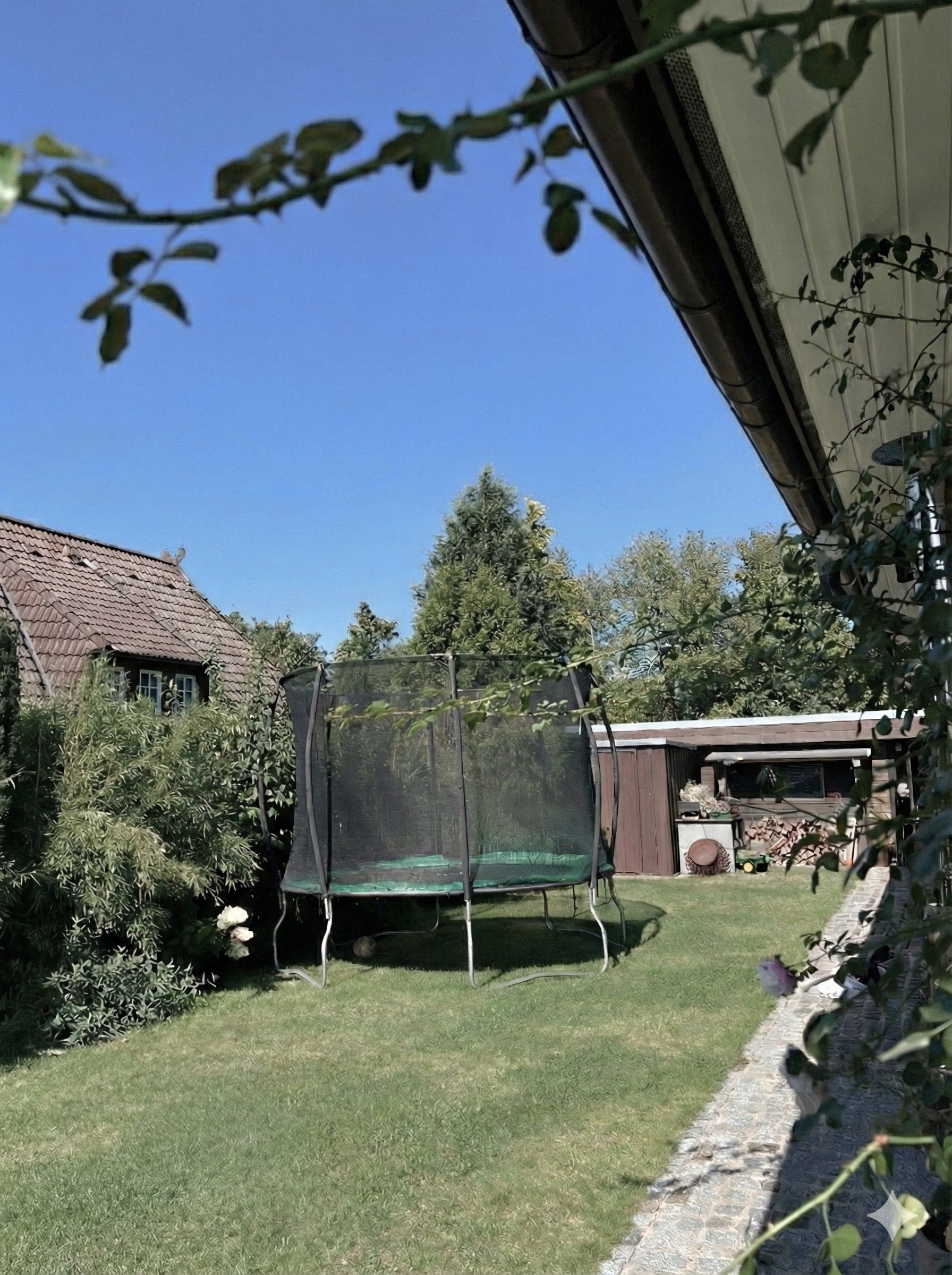 En trädgård med en studsmatta, ett trähus och ett hus med ett sluttande tak.