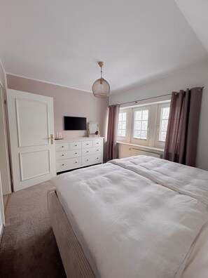 A bedroom with a bed, a dresser, a television, and a window with curtains.