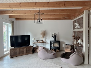 A modern living room with a flat-screen TV, wooden beams, a fireplace, and bean bags.