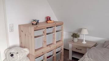 A bedroom with a bed, a wooden storage unit with drawers, a white teddy bear, a lamp, and a small plant.