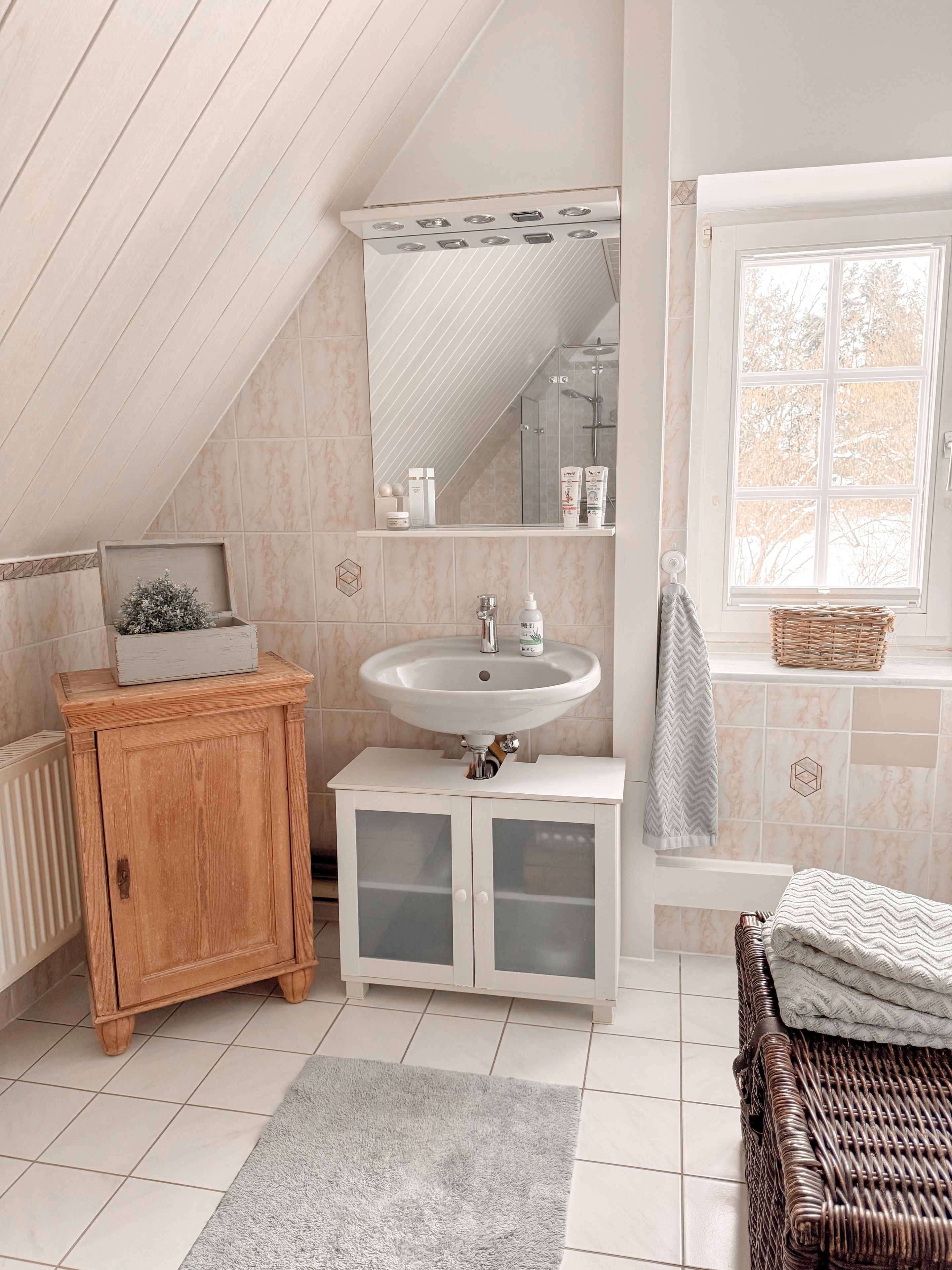 Ein Badezimmer mit Holzschrank, Waschbecken, Spiegel und Fenster.