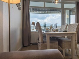A room with a dining table set for breakfast, wicker chairs, a view of the sea, and a window with a curtain.
