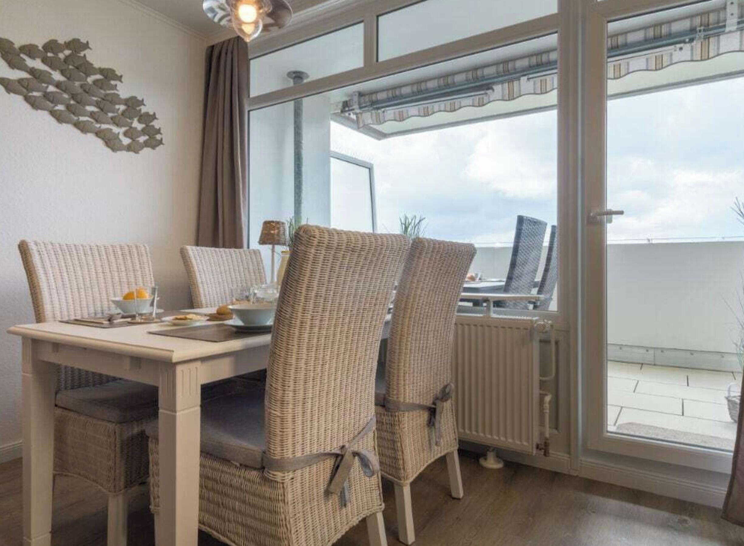 A dining area with wicker chairs and a table, a window with a view, and a radiator.