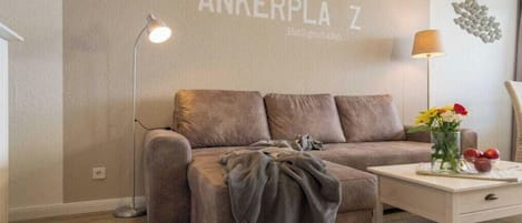 En moderne stue med sofa, sofabord, lampe og en væg med teksten 'ANKERPLA Z'.