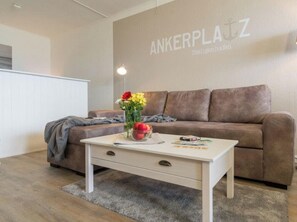 A modern living room with a brown sofa, a white coffee table with a vase of flowers, and a wall with the text 'ANKERPLATZ.' - Holiday Apartment With 3 Bedrooms (Heiligenhafen)