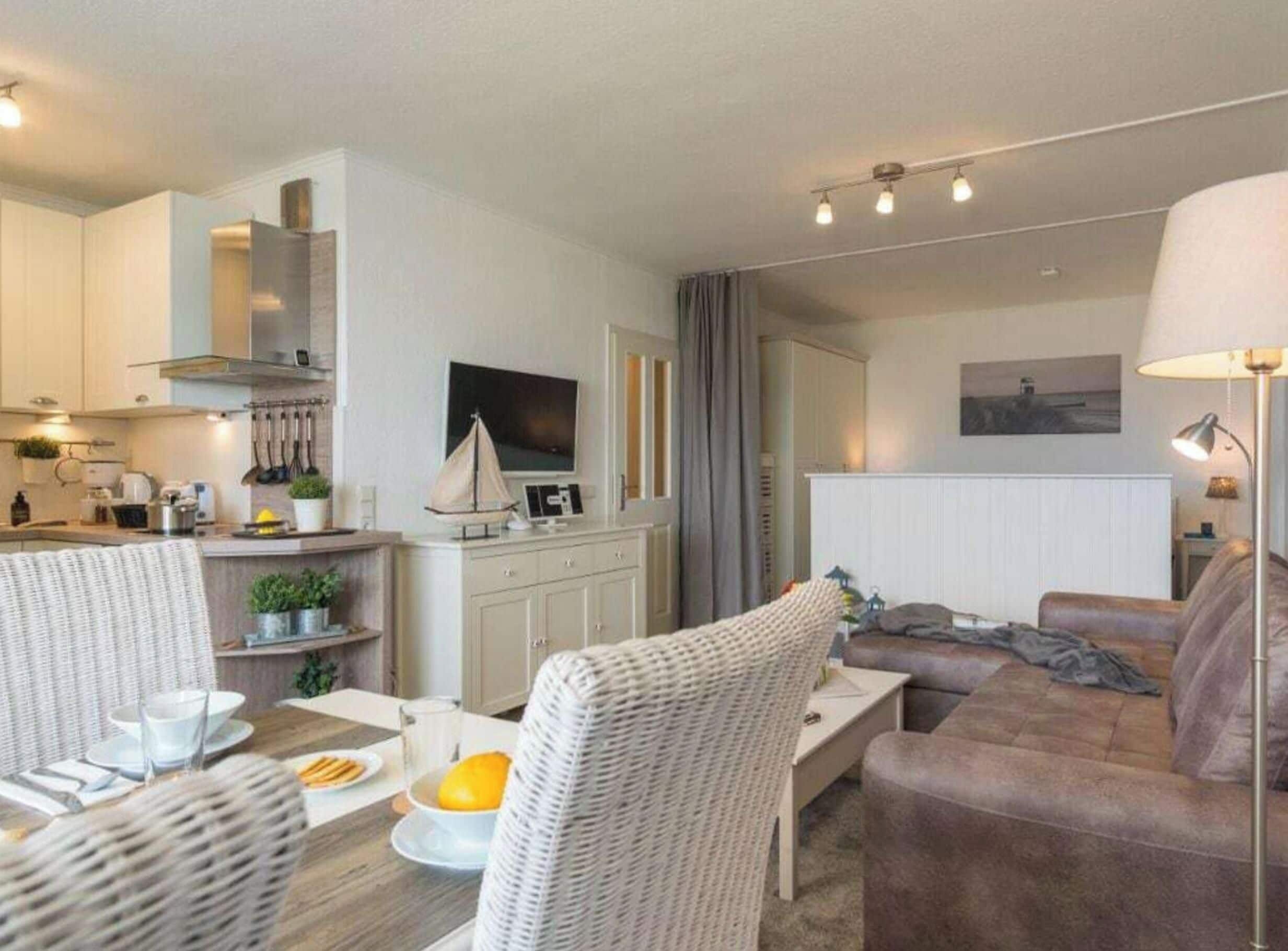 Ein modernes Wohnzimmer mit Sofa, Esstisch mit Stühlen, Küchenzeile mit Herd und Fernseher.