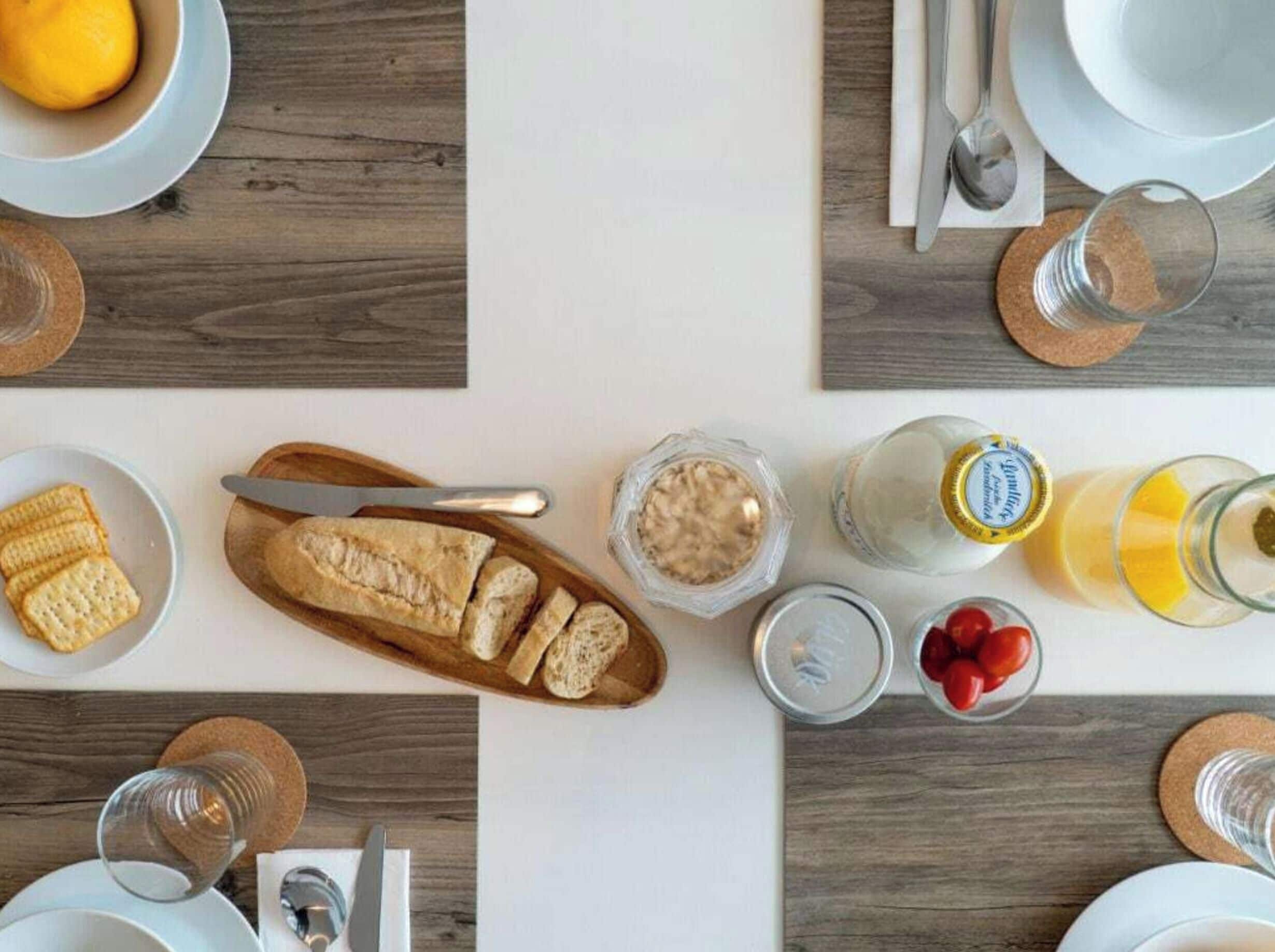 A breakfast setting with bread, cereal, fruit, and beverages on a wooden table.