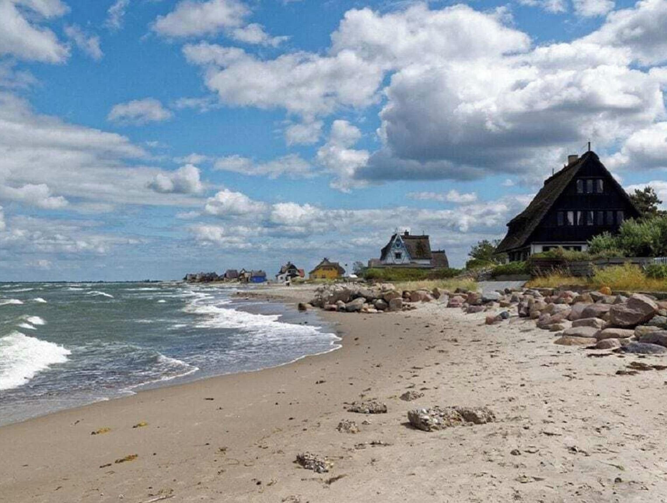 Een strand met een huis met rieten dak en een rotsachtige kustlijn.