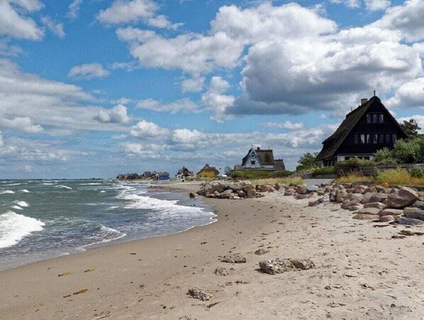 A beach with a thatched-roof house and a rocky shoreline. - Holiday Apartment With 3 Bedrooms (Heiligenhafen)