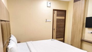 Cama bem arrumada em quarto com cabeceira de madeira, porta fechada e televisão na parede.