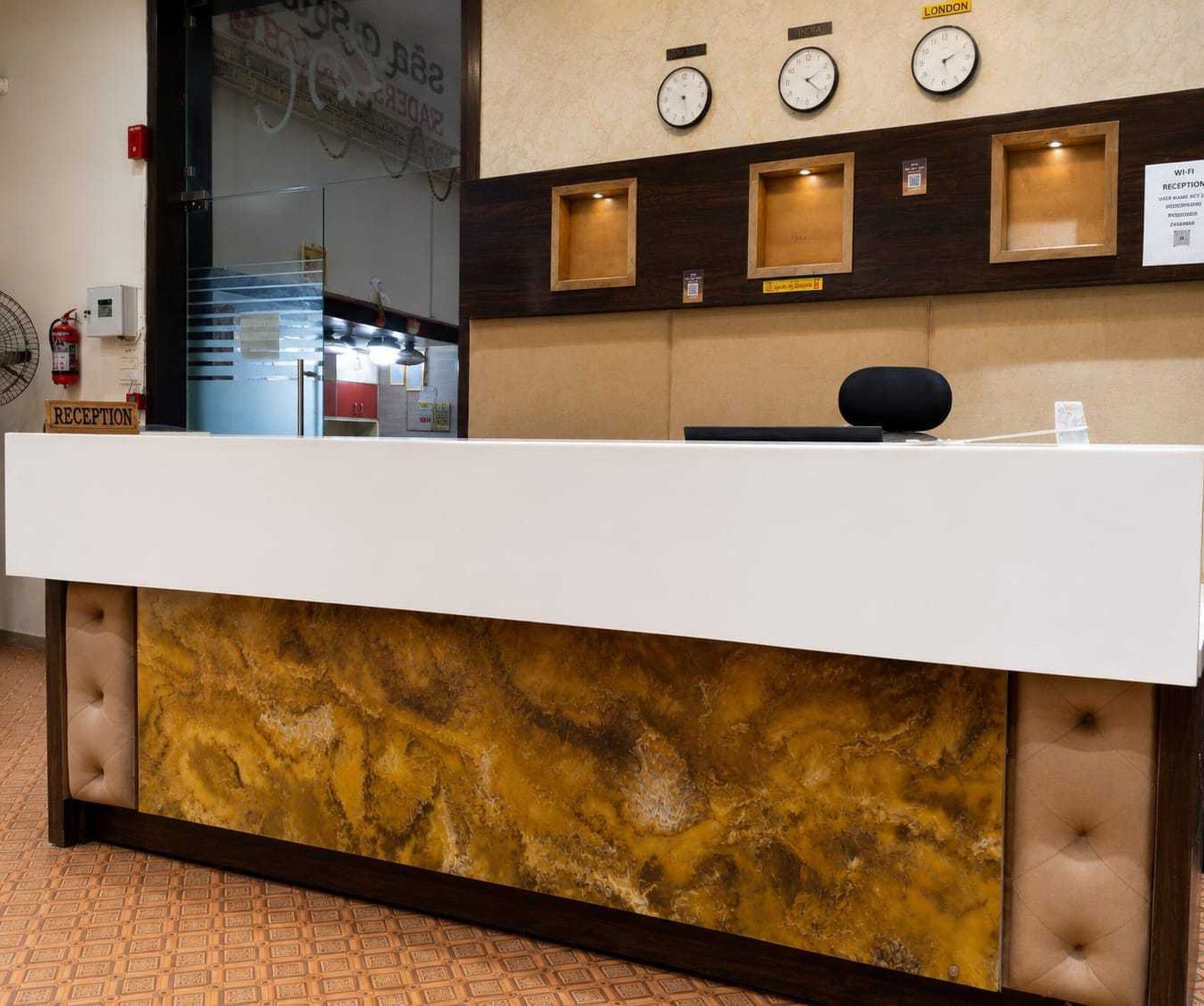 A reception desk with a marble-like front panel, clocks above it, and a fire extinguisher to the left.