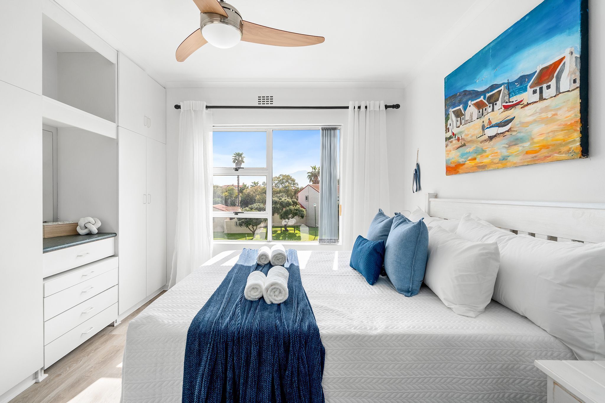 A modern bedroom with a bed, a painting, and a view of the outdoors.