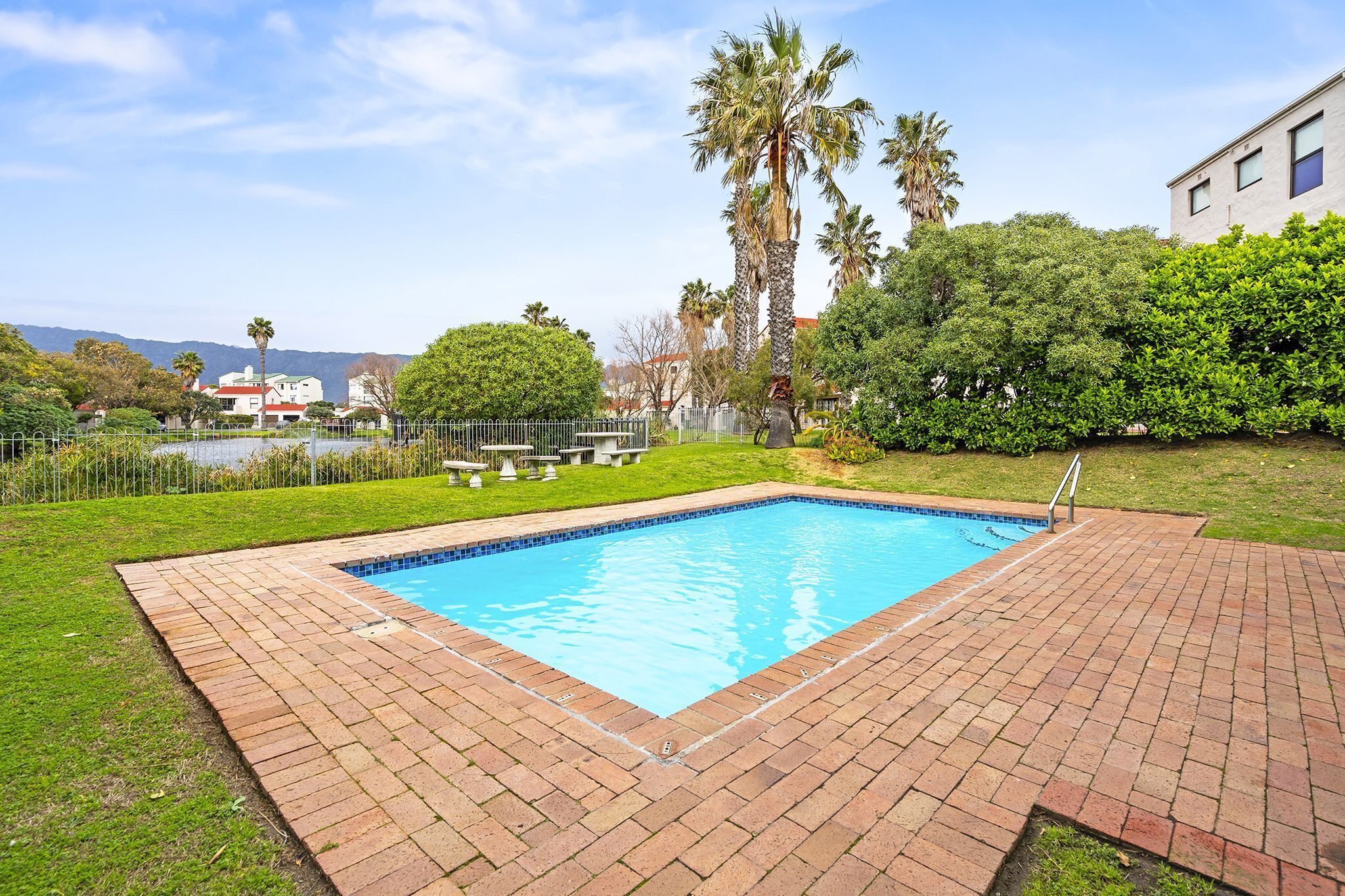 A rectangular swimming pool with a tiled edge, surrounded by a brick patio.