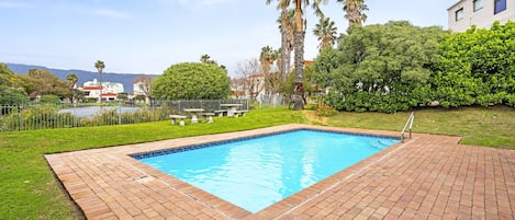 Una piscina rectangular con borde de azulejos, rodeada por un patio de ladrillo.