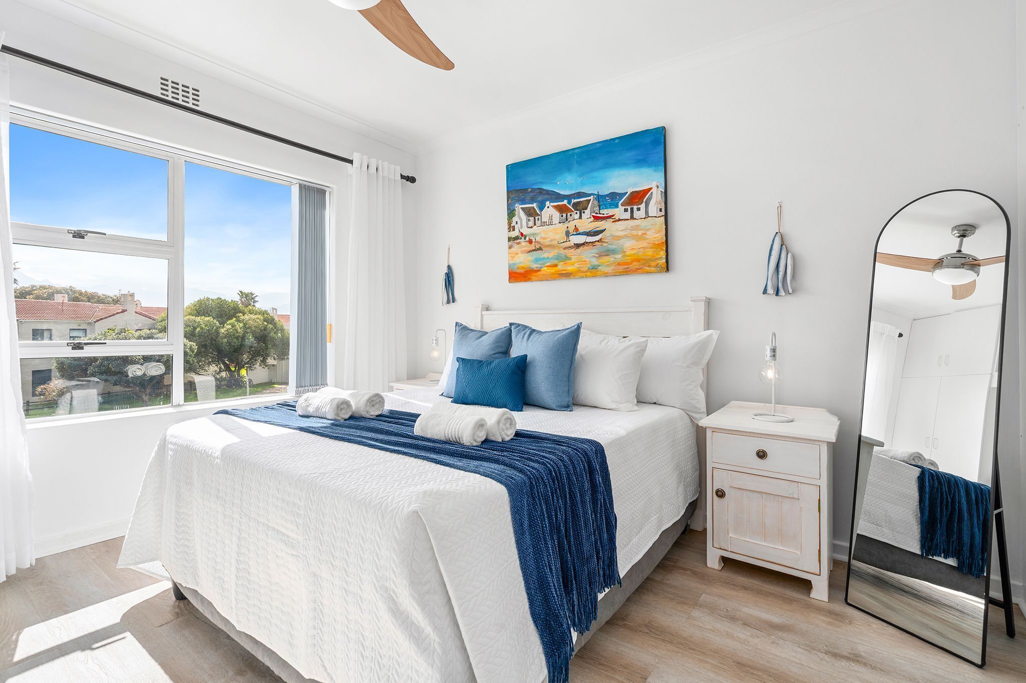 A bedroom with a bed, a nightstand, a mirror, and a painting on the wall.