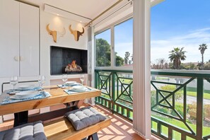 A dining area with a table set for four, a fireplace, and a balcony with a view of palm trees. - Annies Haven at Greenways Golf Estate (Cape Town)