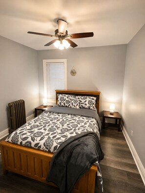 A bedroom with a wooden bed, a ceiling fan, a radiator, and two bedside lamps.