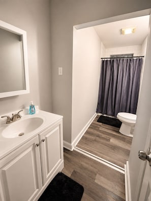 A bathroom with a white vanity, a mirror, a sink, a toilet, and a shower curtain.