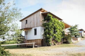 Une maison en bois à deux étages, avec une façade blanche, un balcon en bois et un jardin.