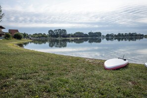 Un lac paisible aux rives verdoyantes, une planche à pagaie et un petit bâtiment en arrière-plan.