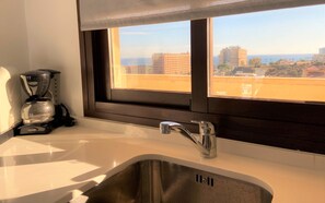A kitchen with a stainless steel sink, a coffee maker, and a window with a view of buildings and a clear sky. - Aloha Playa Deluxe: Wi-Fi, Swimming Pools, and Parking (Benalmádena)